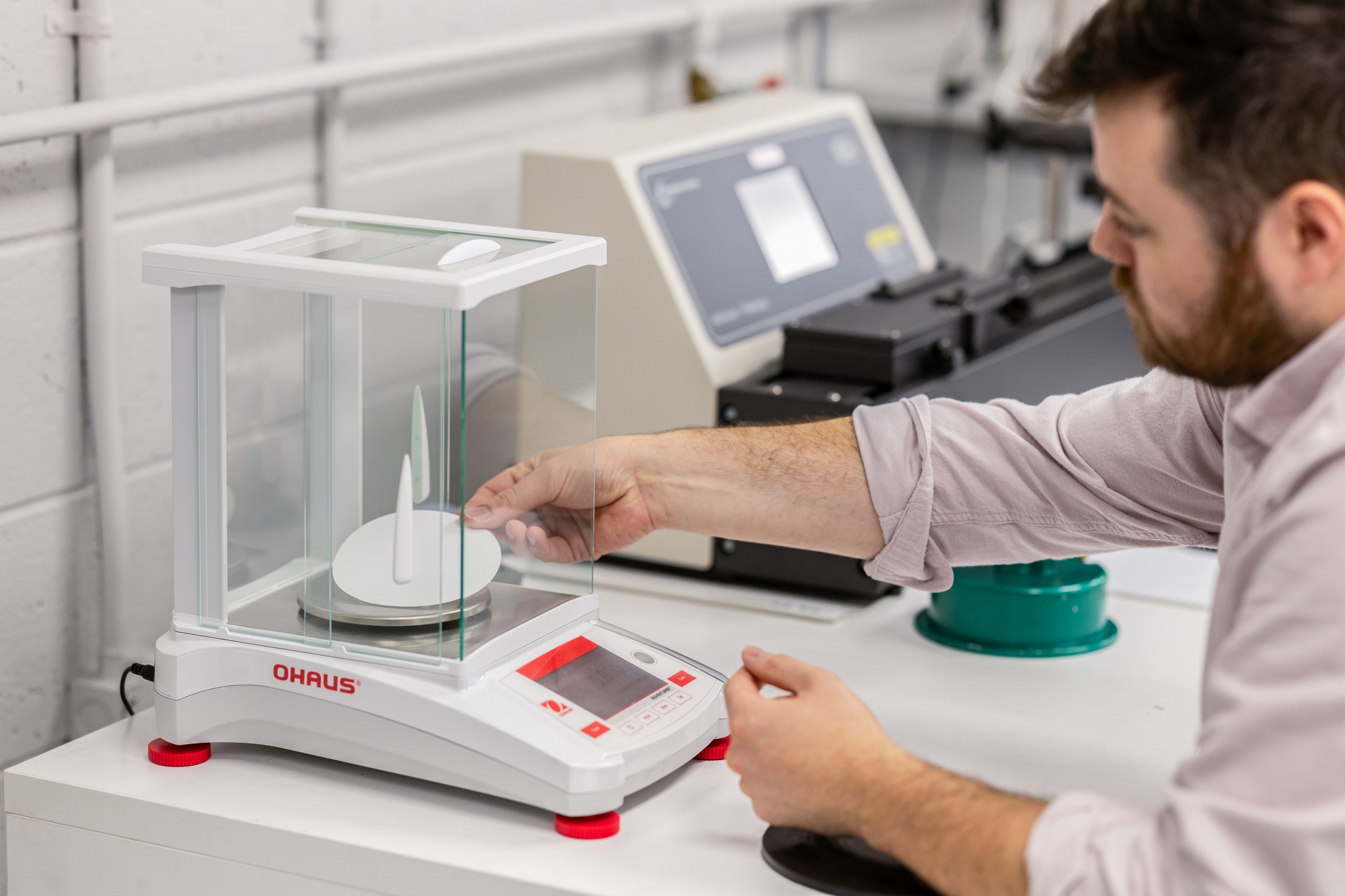 Hands placing a sample on an analytical balance during adhesive coat-weight evaluation